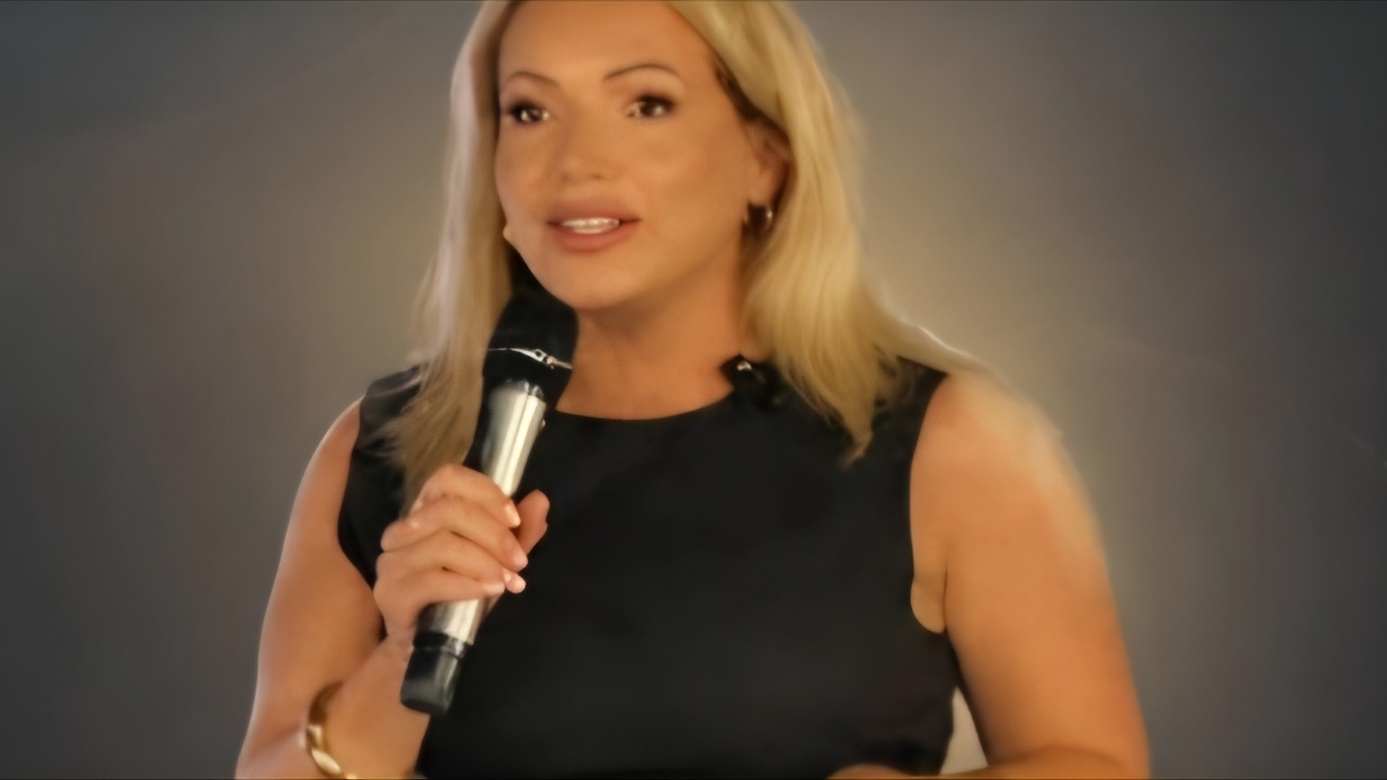 Joanne Kimberley speaking into a microphone on stage, smiling as she addresses an audience