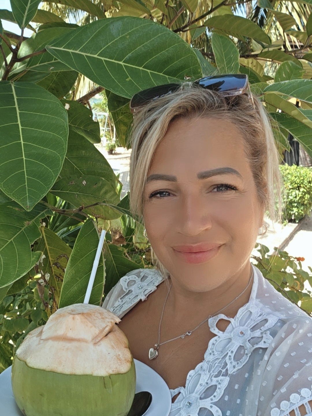 Joanne Kimberley holding a fresh green coconut drink against tropical foliage
