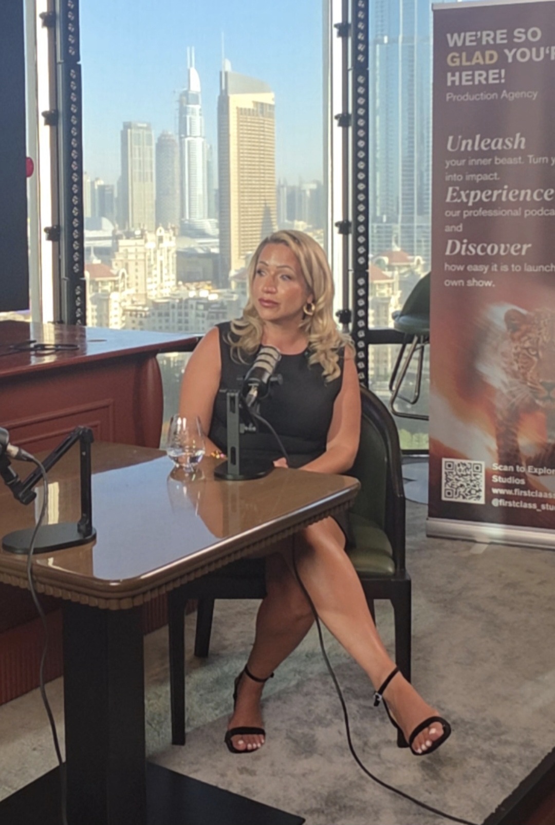 Joanne Kimberley at a podcast studio desk with a microphone and a city skyline behind her