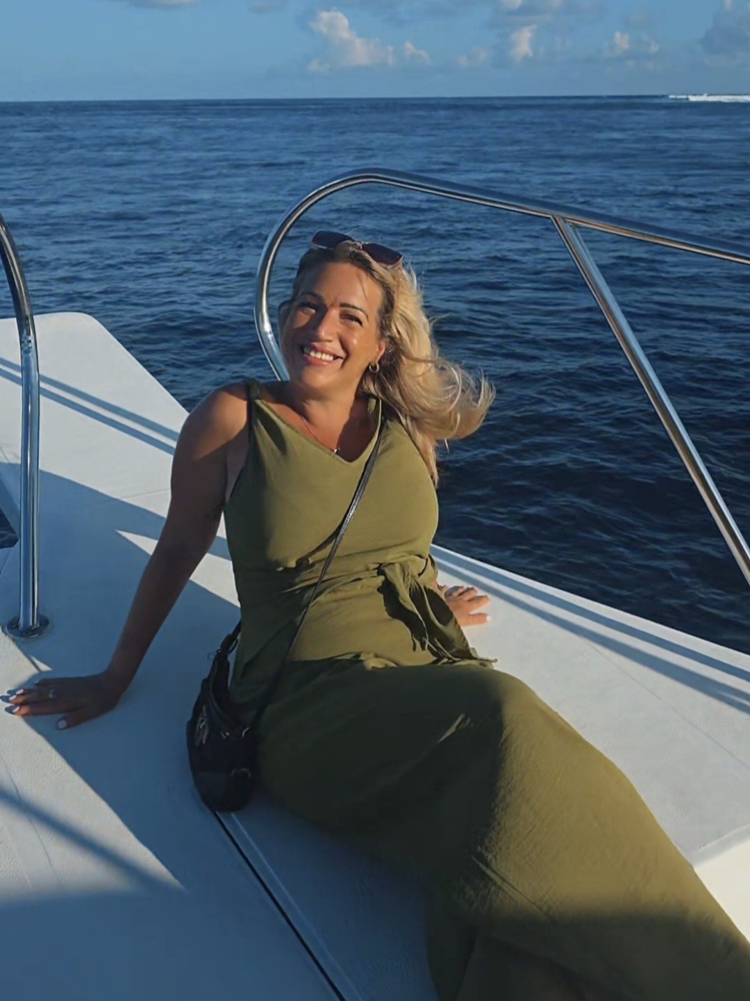 Joanne Kimberley in an olive dress relaxing on the deck of a boat on open blue water